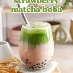 Strawberry matcha boba in a glass with straw and matcha whisk on the side.