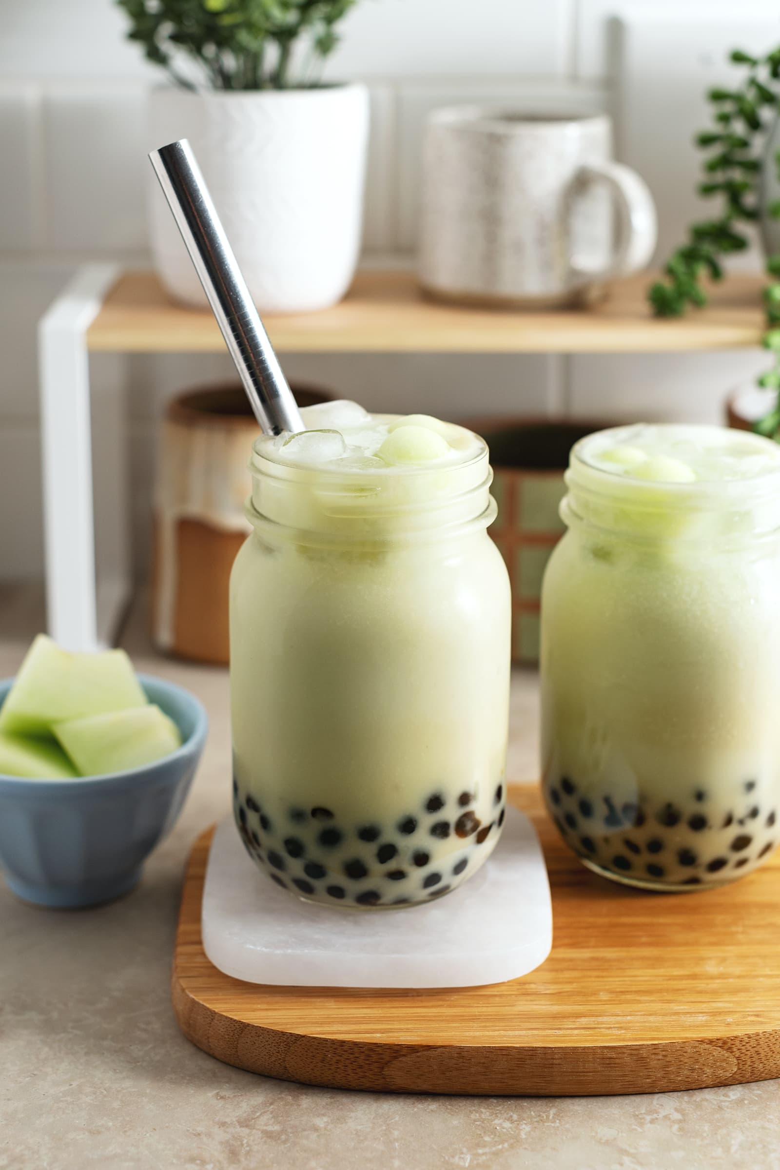 Two glasses of honeydew bubble tea on a wooden platter.