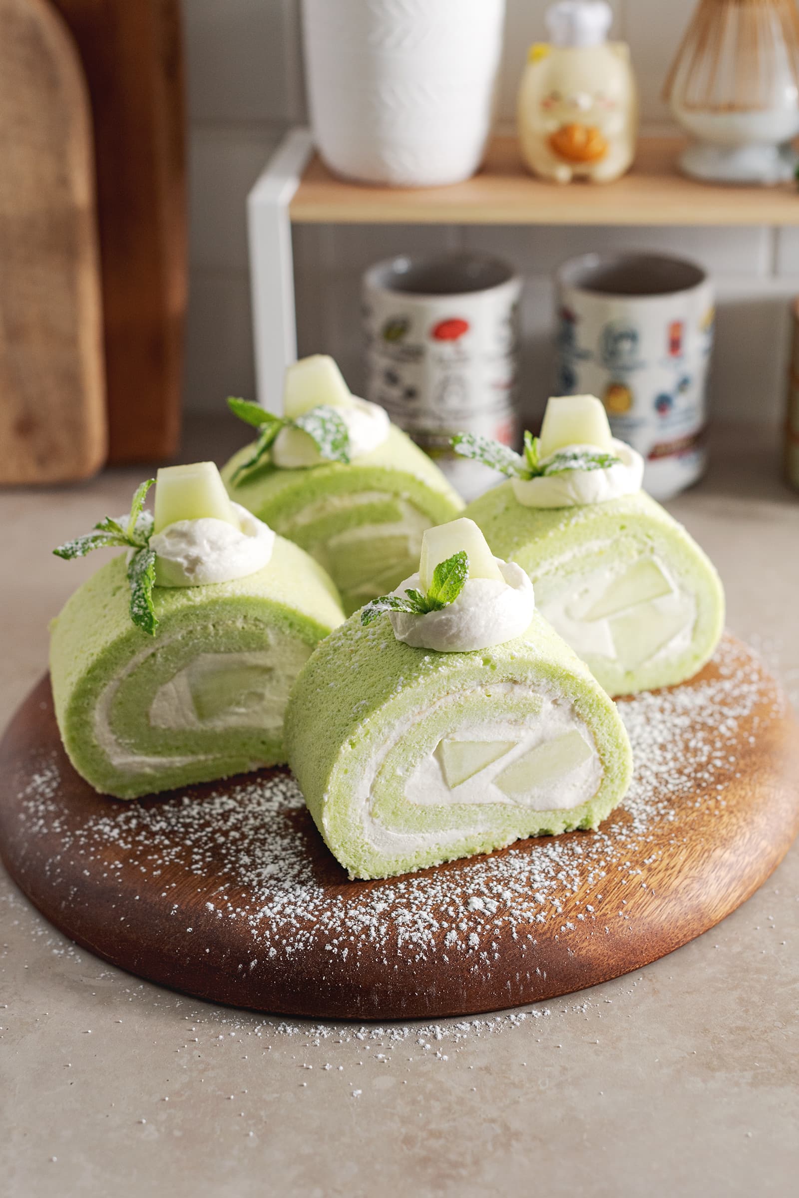 Four slices of honeydew roll cake sprinkled with powdered sugar on a wooden platter.
