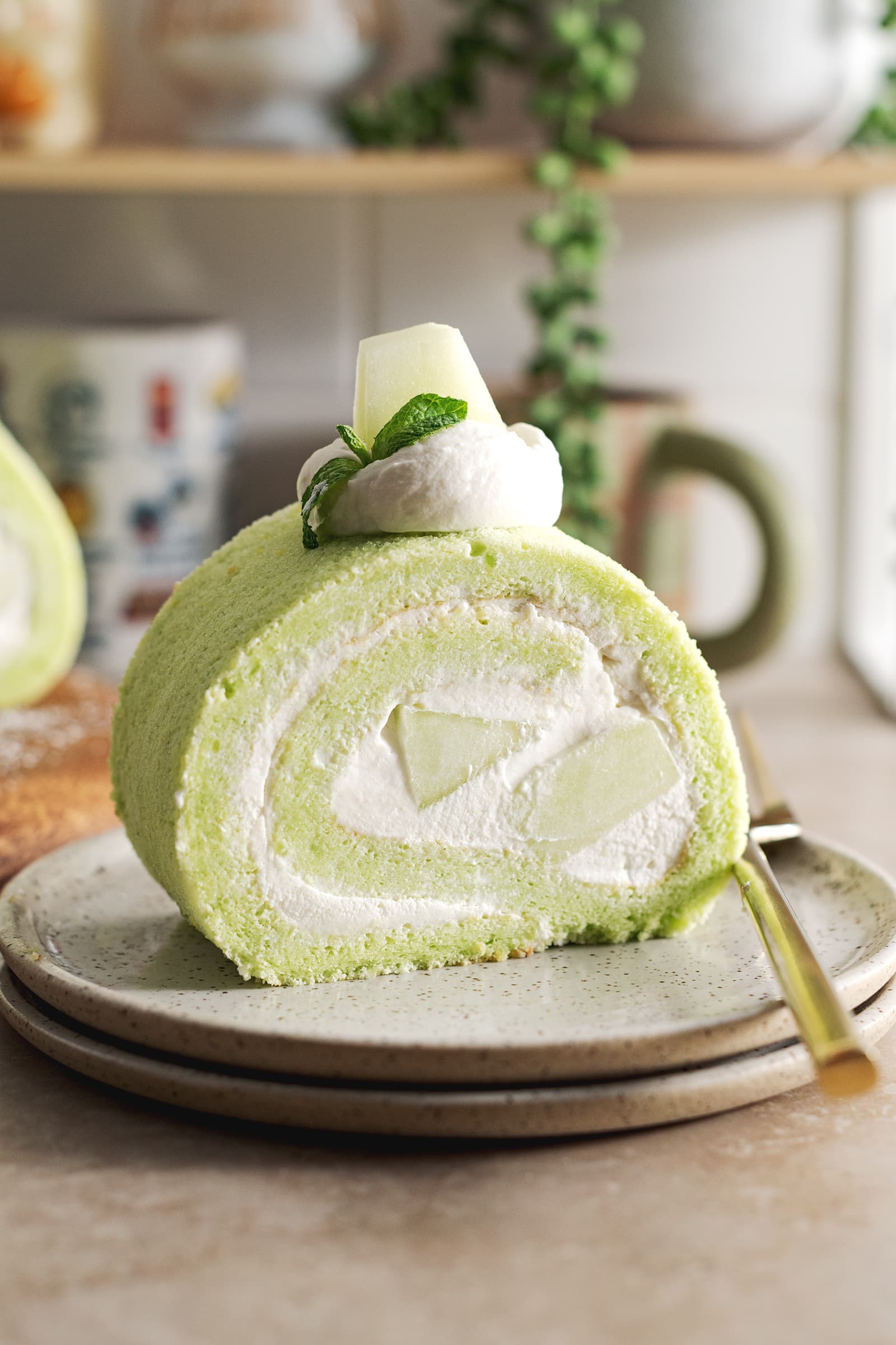 A slice of honeydew roll cake on a stack of plates.