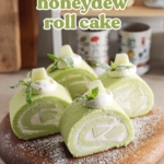 Four slices of honeydew roll cake sprinkled with powdered sugar on a wooden platter.