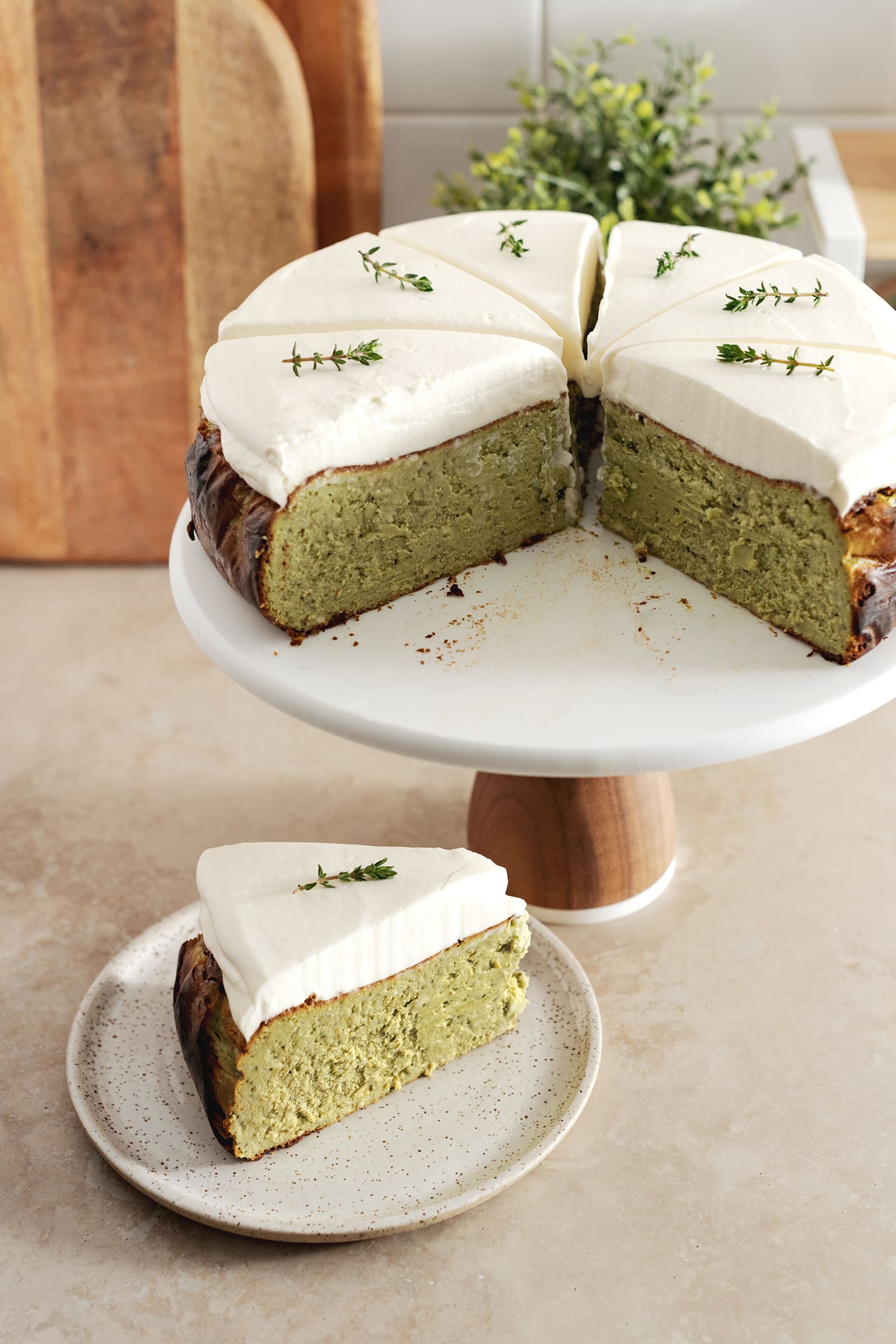 A slice of matcha basque cheesecake on a plate and the rest of the cake on a cake stand.