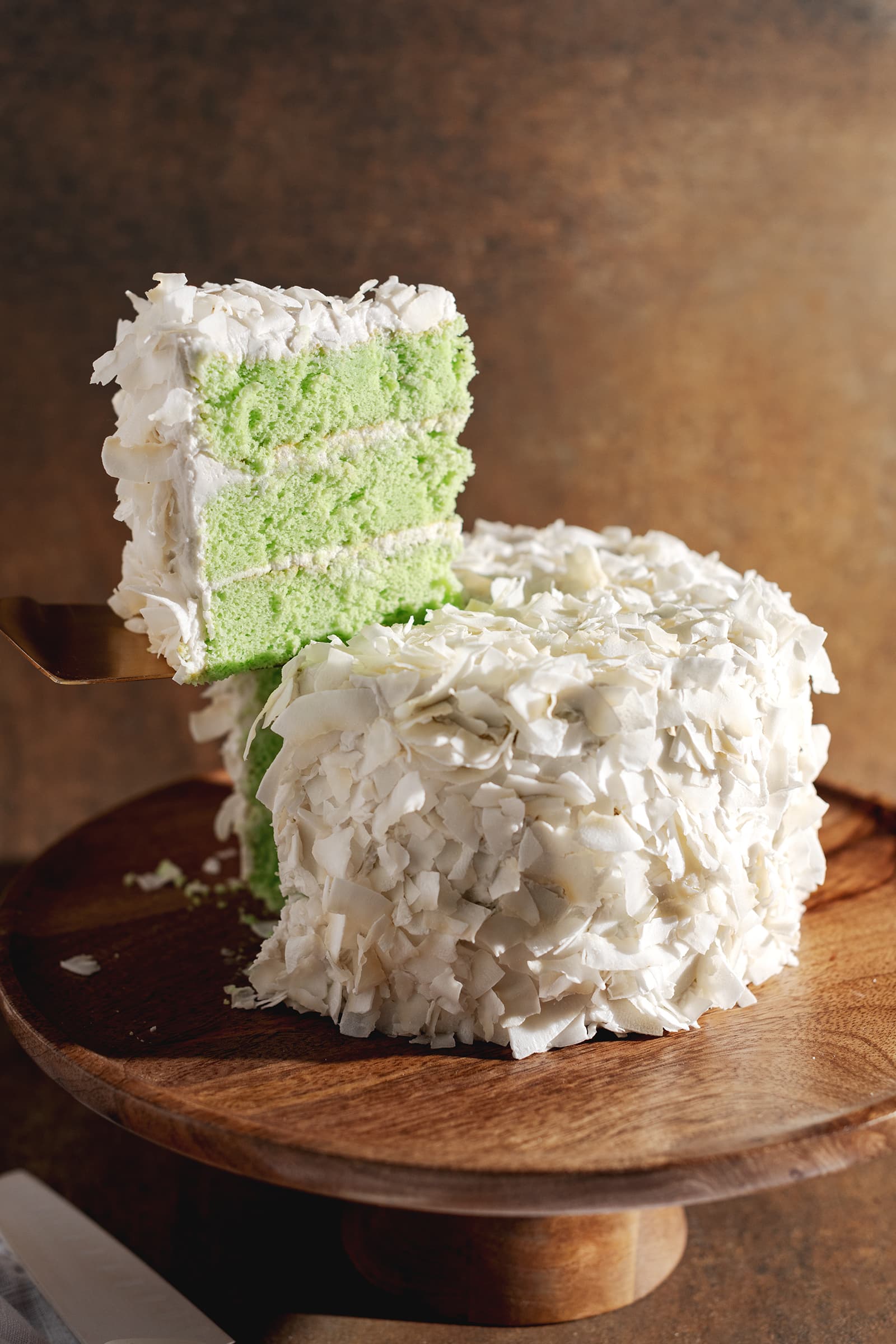 A slice of pandan coconut cake being lifted from the whole cake with a cake server.