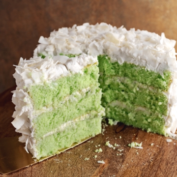 A slice of pandan coconut cake in front of half of a cake in the background.