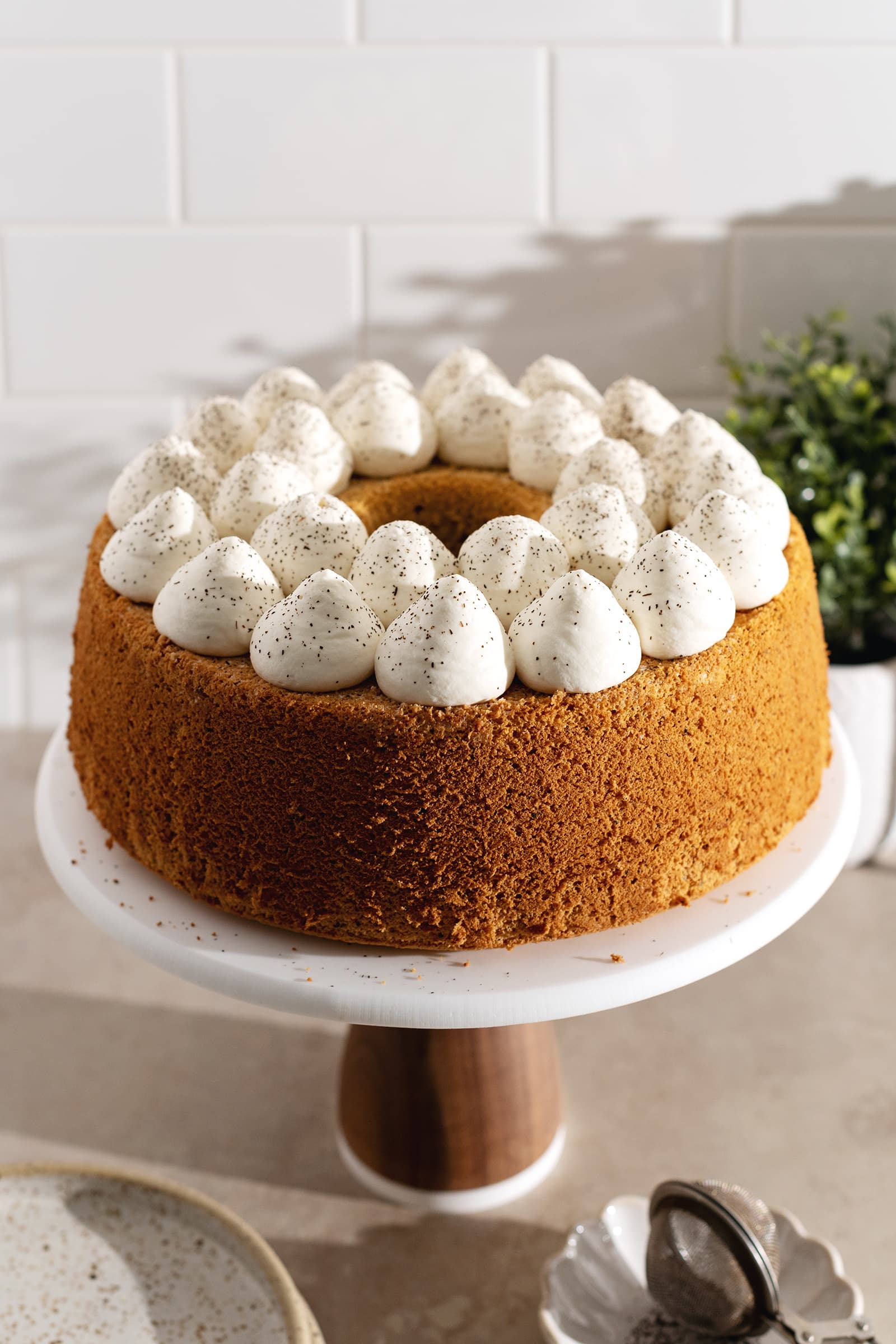 A chiffon cake topped with dollops of whipped cream on a cake stand.
