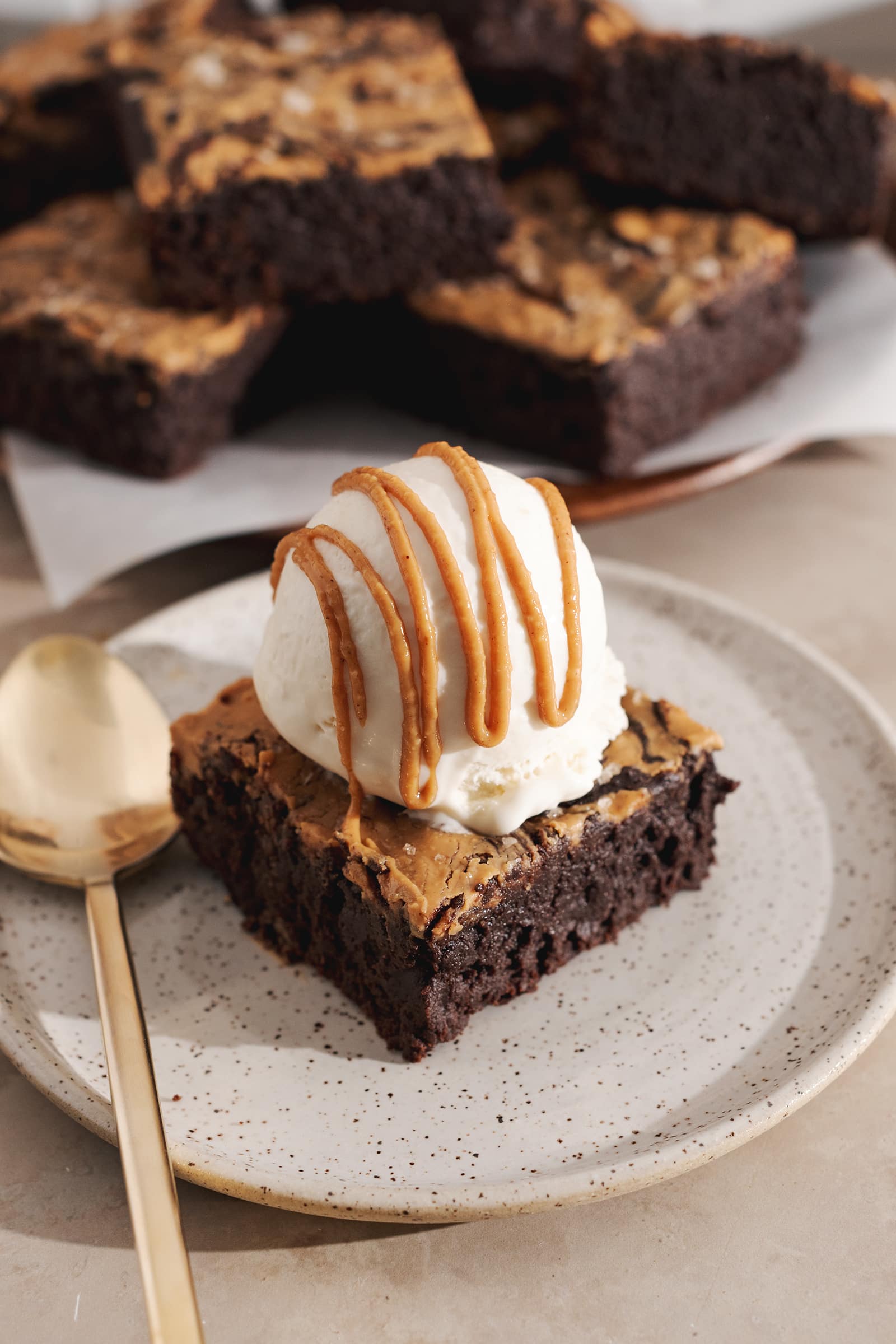 A brownie square topped with a scoop of vanilla ice cream and drizzled with peanut butter on a plate.