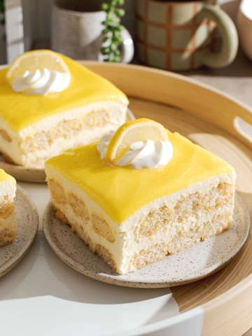 Square slices of limoncello tiramisu on a round tray with layers of ladyfingers, mascarpone, and lemon curd.