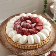 Strawberry custard tart topped with dollops of whipped cream and layers of strawberries on a wooden plate.