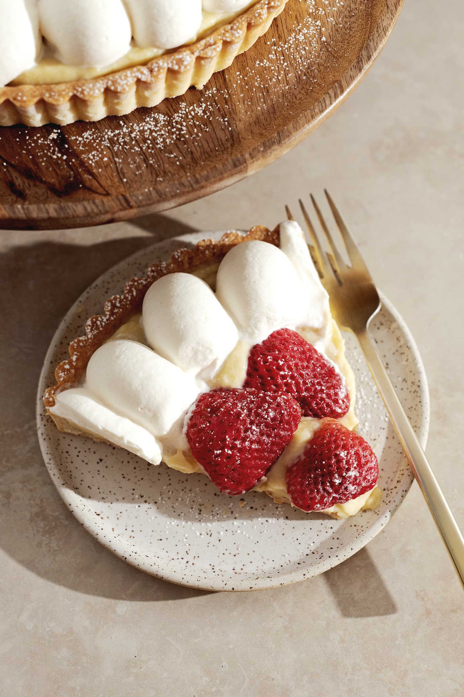 A slice of strawberry tart on a speckled plate with a gold fork.