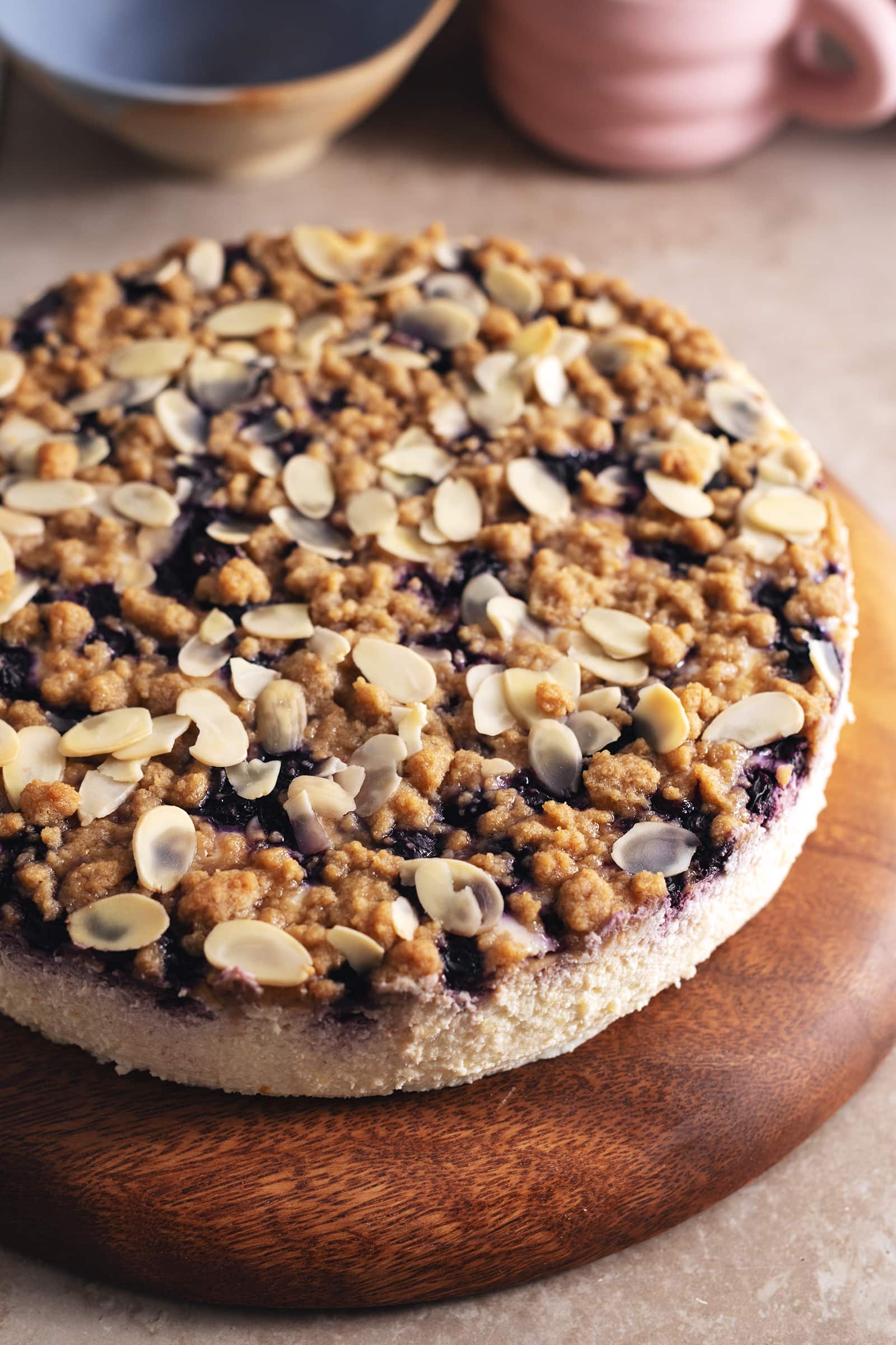 A blueberry crumble cheesecake on a wooden platter.