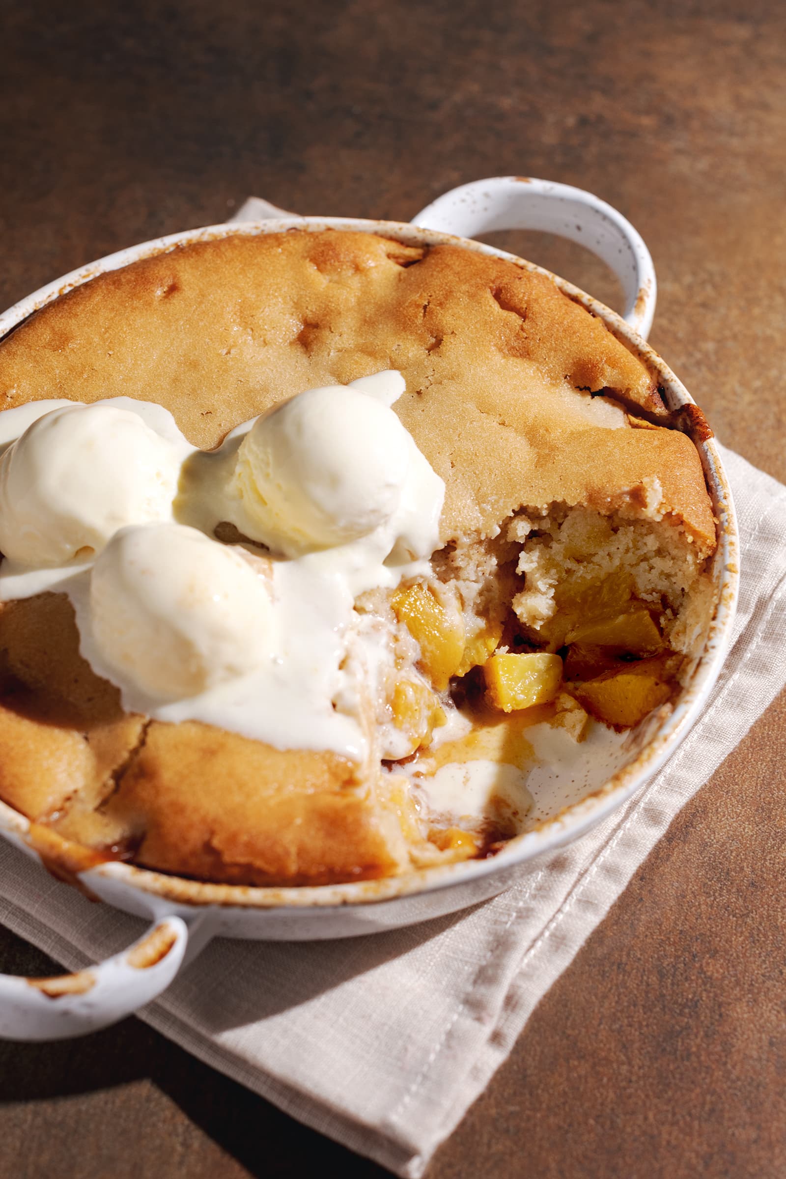 A dish of peach cobbler with a scoop taken out of it to show the peach filling inside.