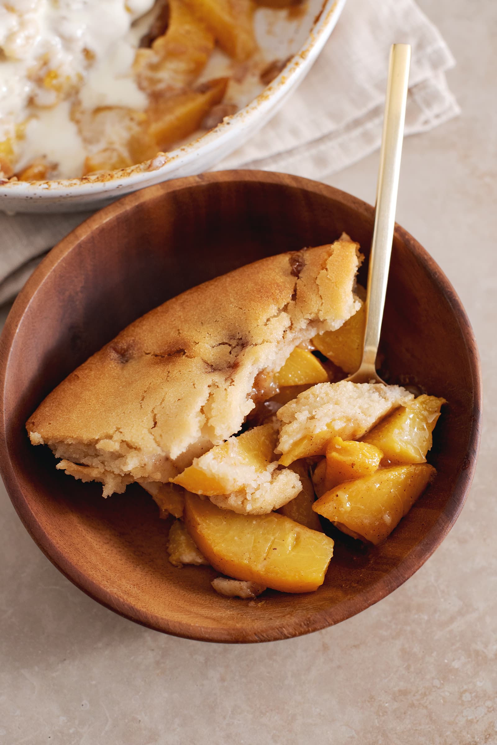 A slice of peach cobbler in a wooden bowl with a spoon.
