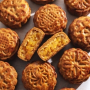 A pineapple mooncake cut in half to show filling inside in the middle of several other mooncakes.