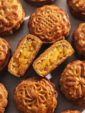 A pineapple mooncake cut in half to show filling inside in the middle of several other mooncakes.