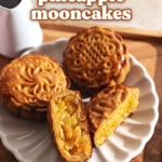 A pineapple mooncake cut in half on a plate with two other mooncakes.