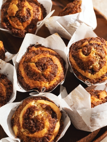 Several cinnamon roll muffins on a wooden platter.
