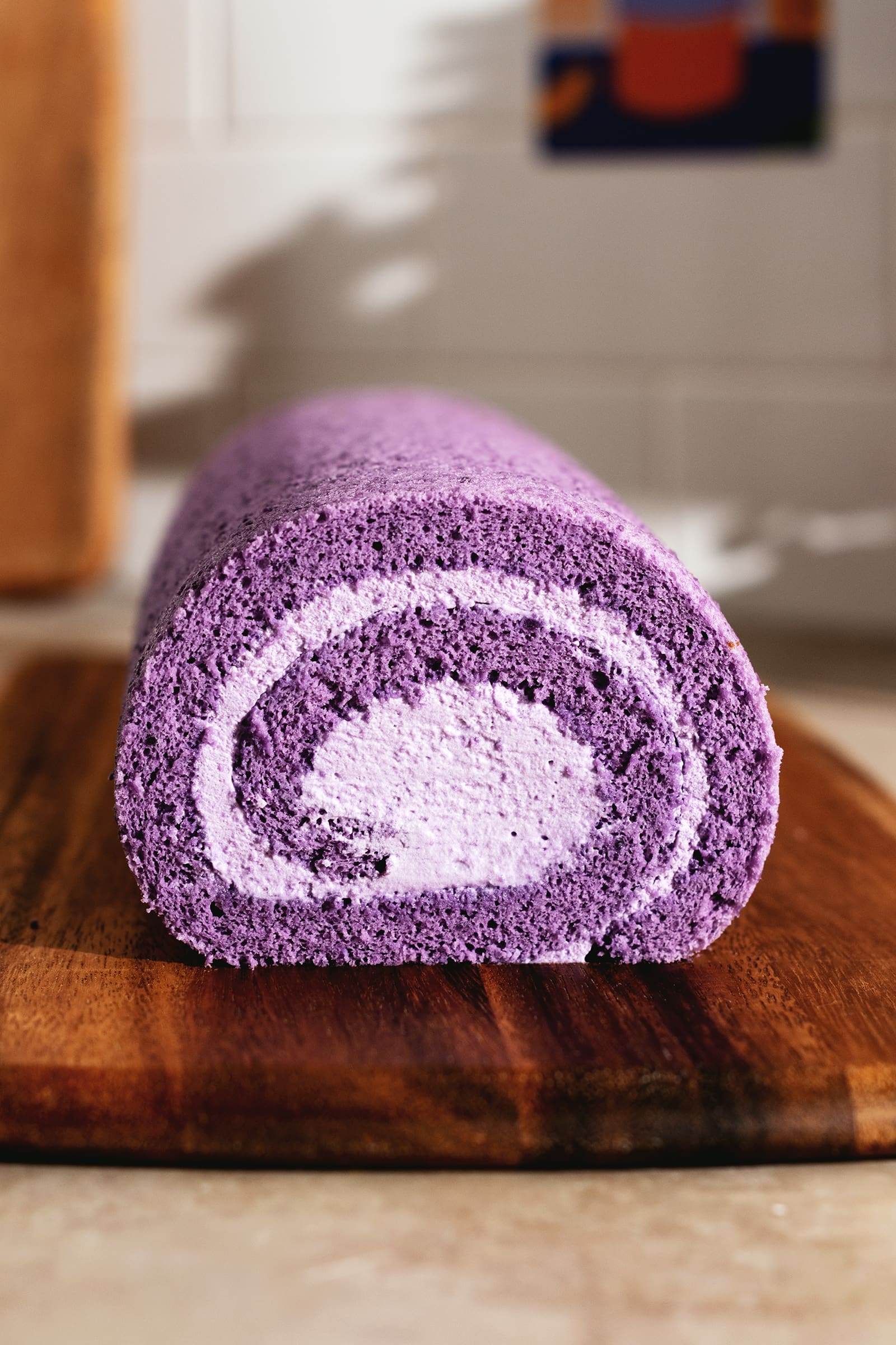 Cross section view of a purple ube roll cake on a wooden board.