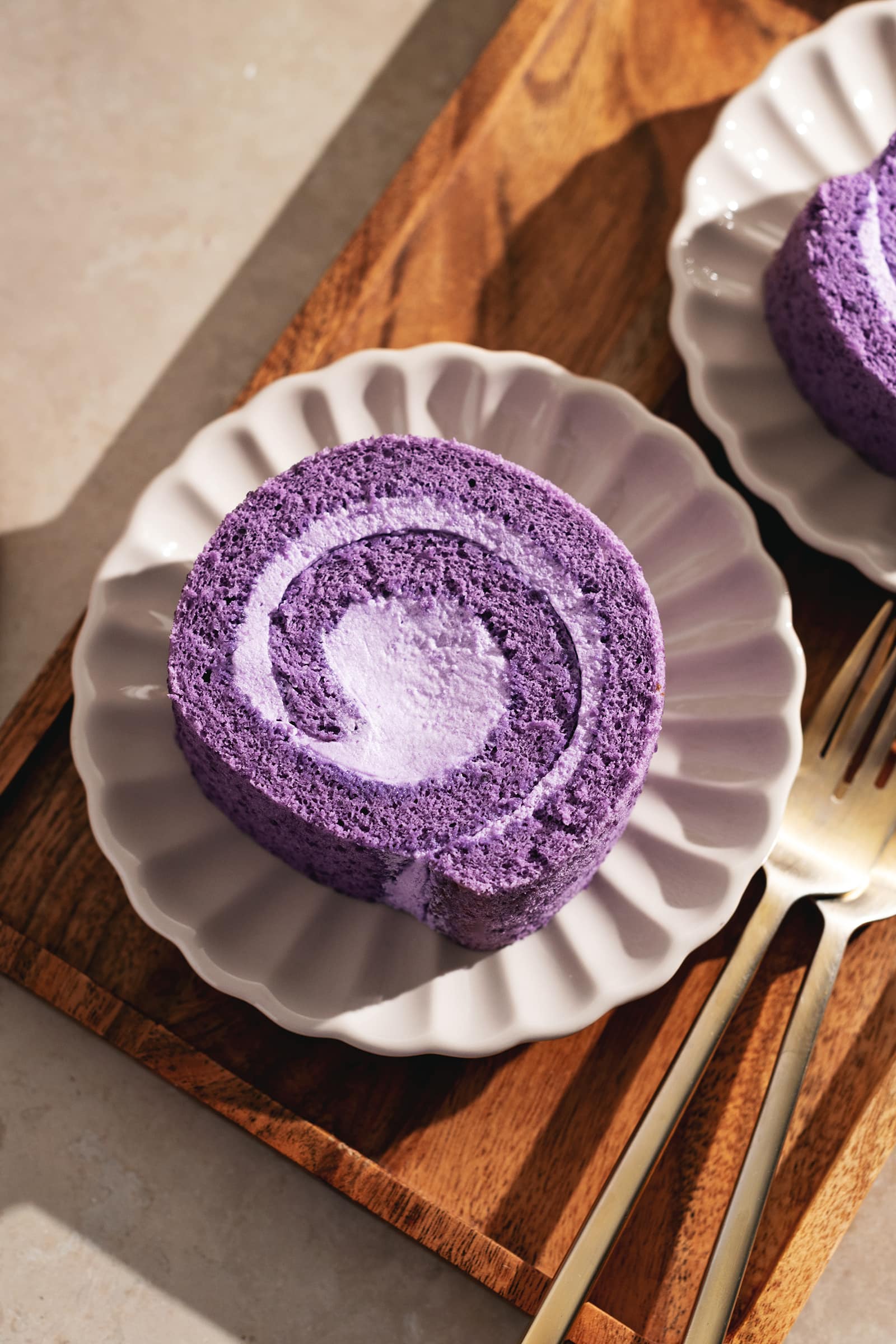 Top down view of a slice of ube roll cake on a scalloped plate on a wooden tray.