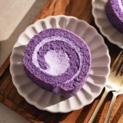 Top down view of a slice of ube roll cake on a scalloped plate on a wooden tray.