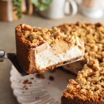 A slice of apple crumble cheesecake lifted up with a cake server.