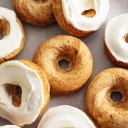 Cinnamon roll donuts scattered on parchment paper, some with cream cheese frosting, some without.