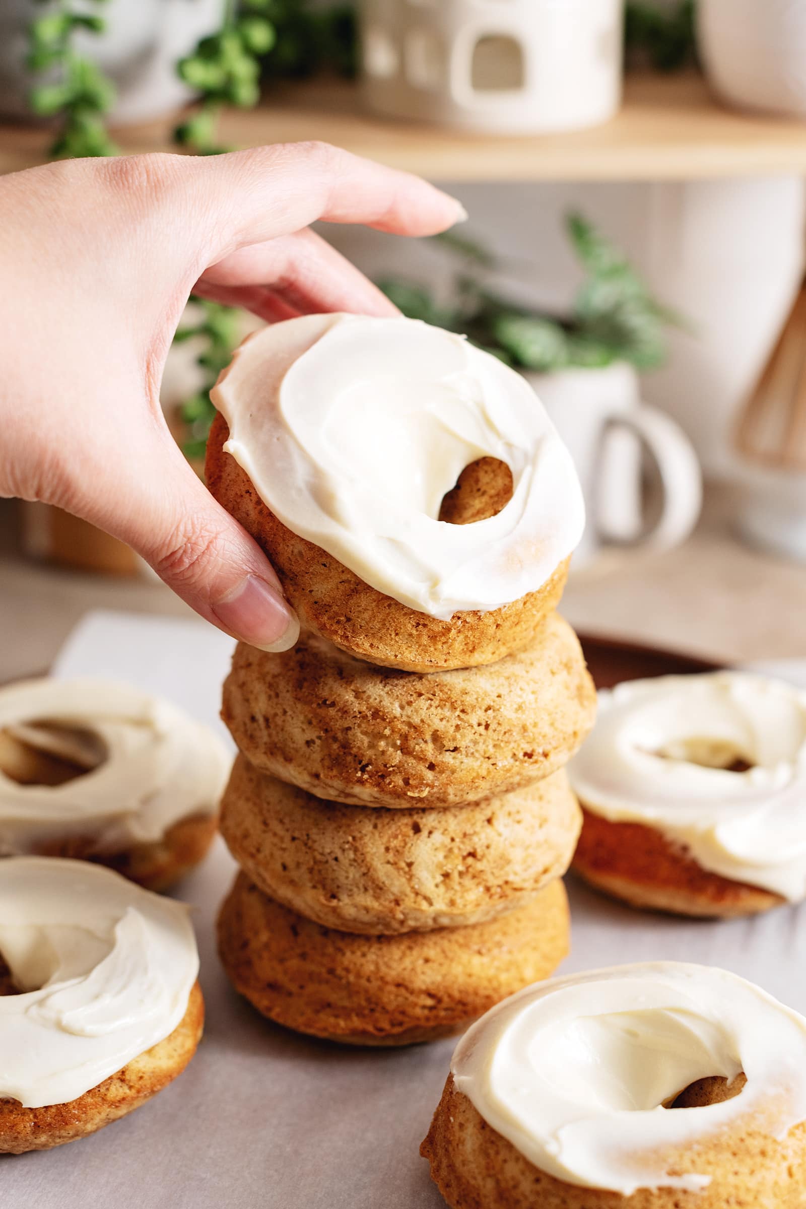 Hand placing a frosted cinnamon roll donut on top of a stack of donuts.