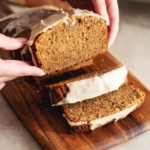 Hands holding a slice of earl grey pound cake above the rest of the loaf.