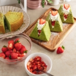 Matcha chiffon cake sandwiches on a wooden platter surrounded by bowls of strawberries.
