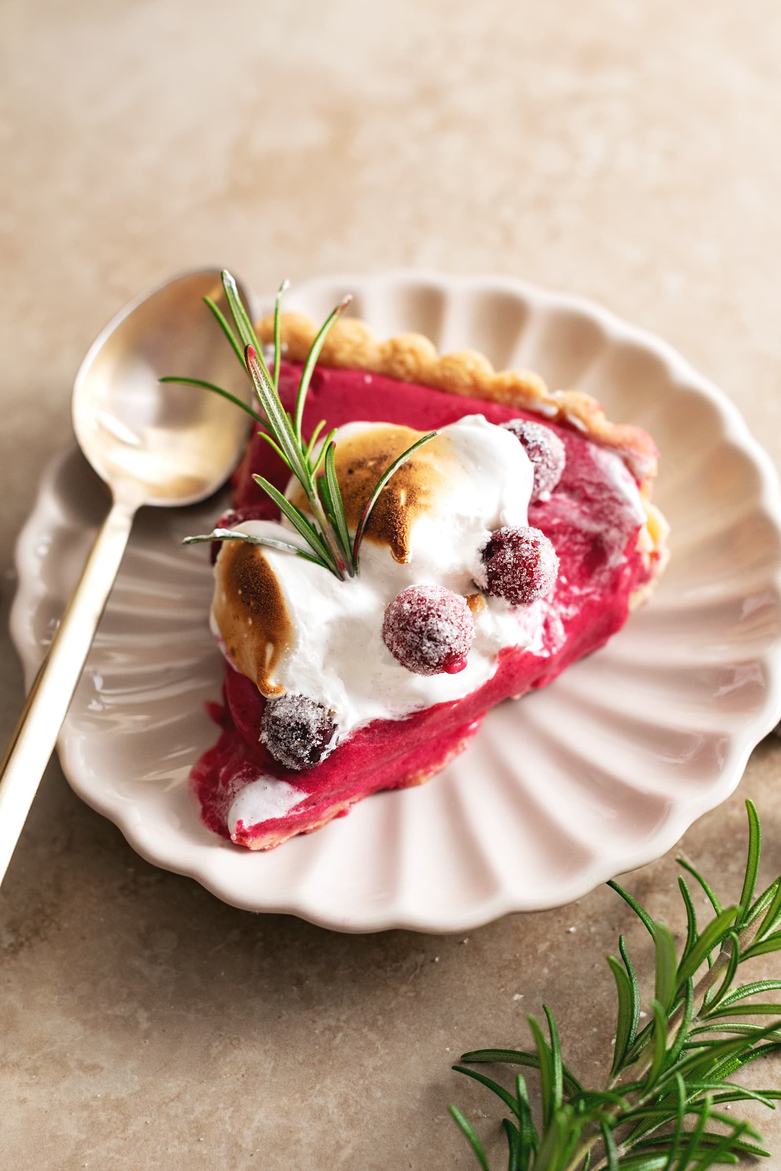 A slice of cranberry meringue tart on a plate with a spoon.