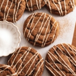 Several gingerbread latte cookies scattered on parchment paper with a small bowl of sugar.