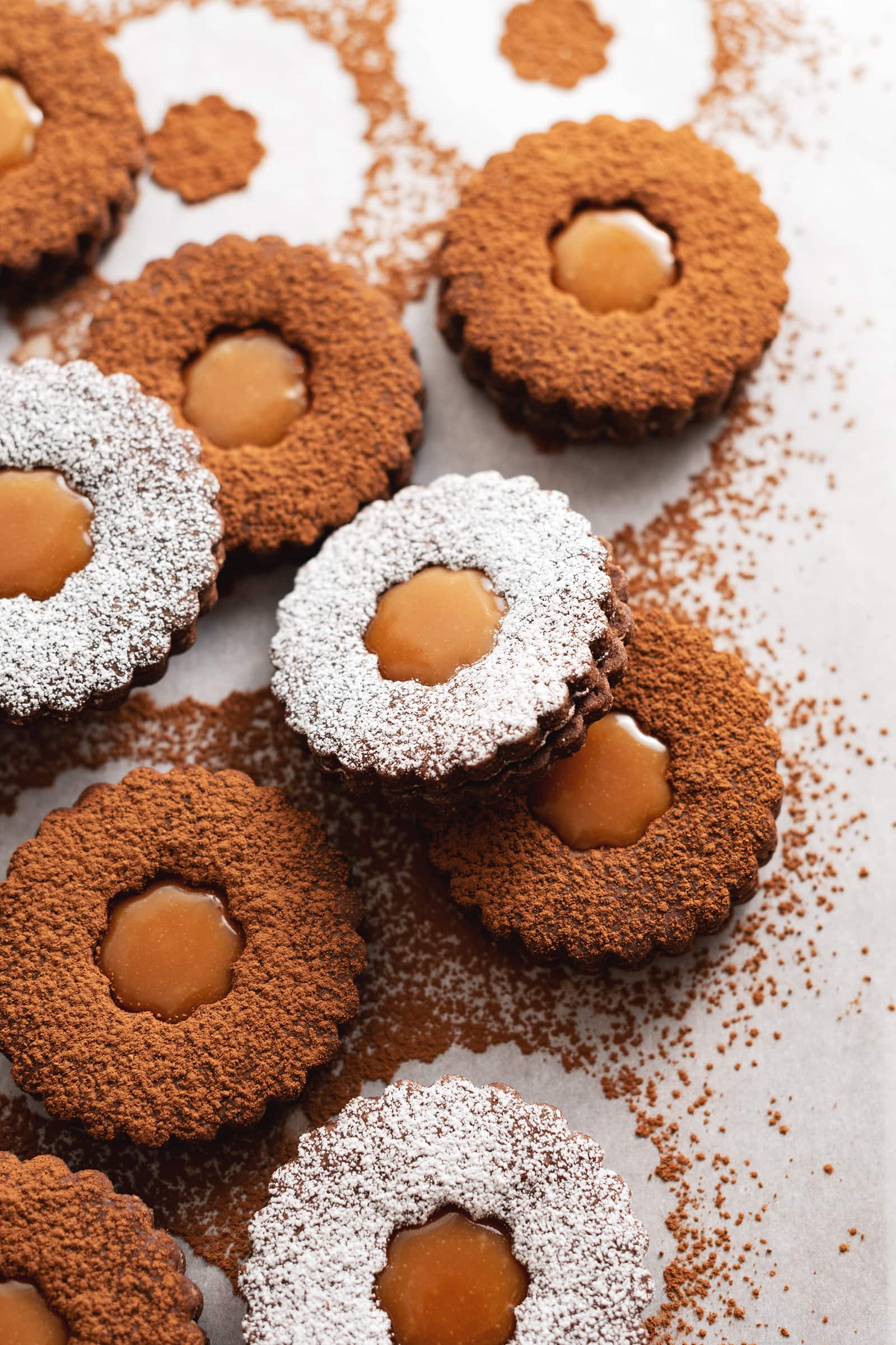 A linzer cookie dusted with powdered sugar resting on another cookie dusted with cocoa powder.
