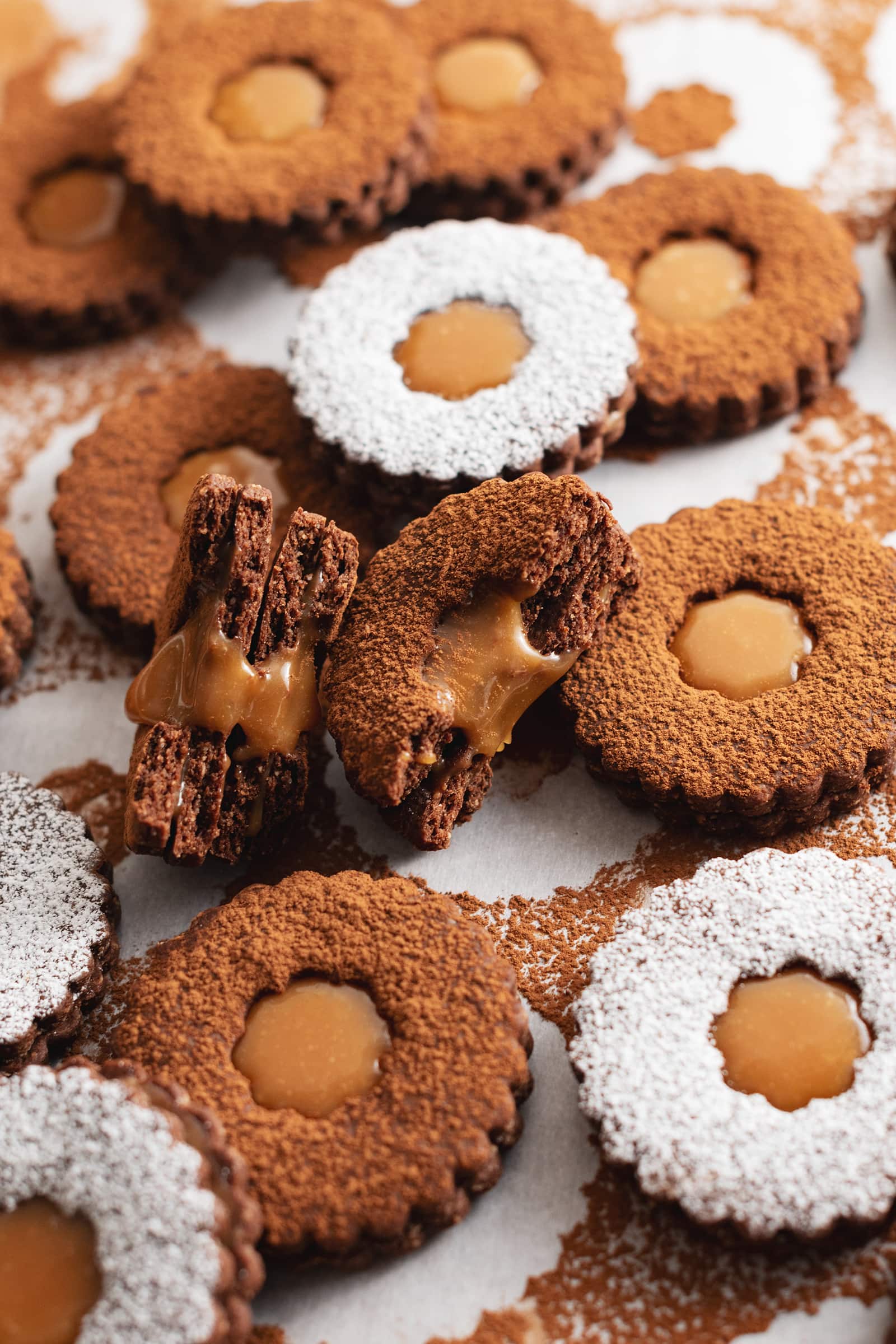 Two salted caramel chocolate linzer cookies split in half to show the gooey caramel filling inside.