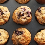 Banana blackberry oatmeal muffins in a muffin pan with some muffins tilted out of the pan.