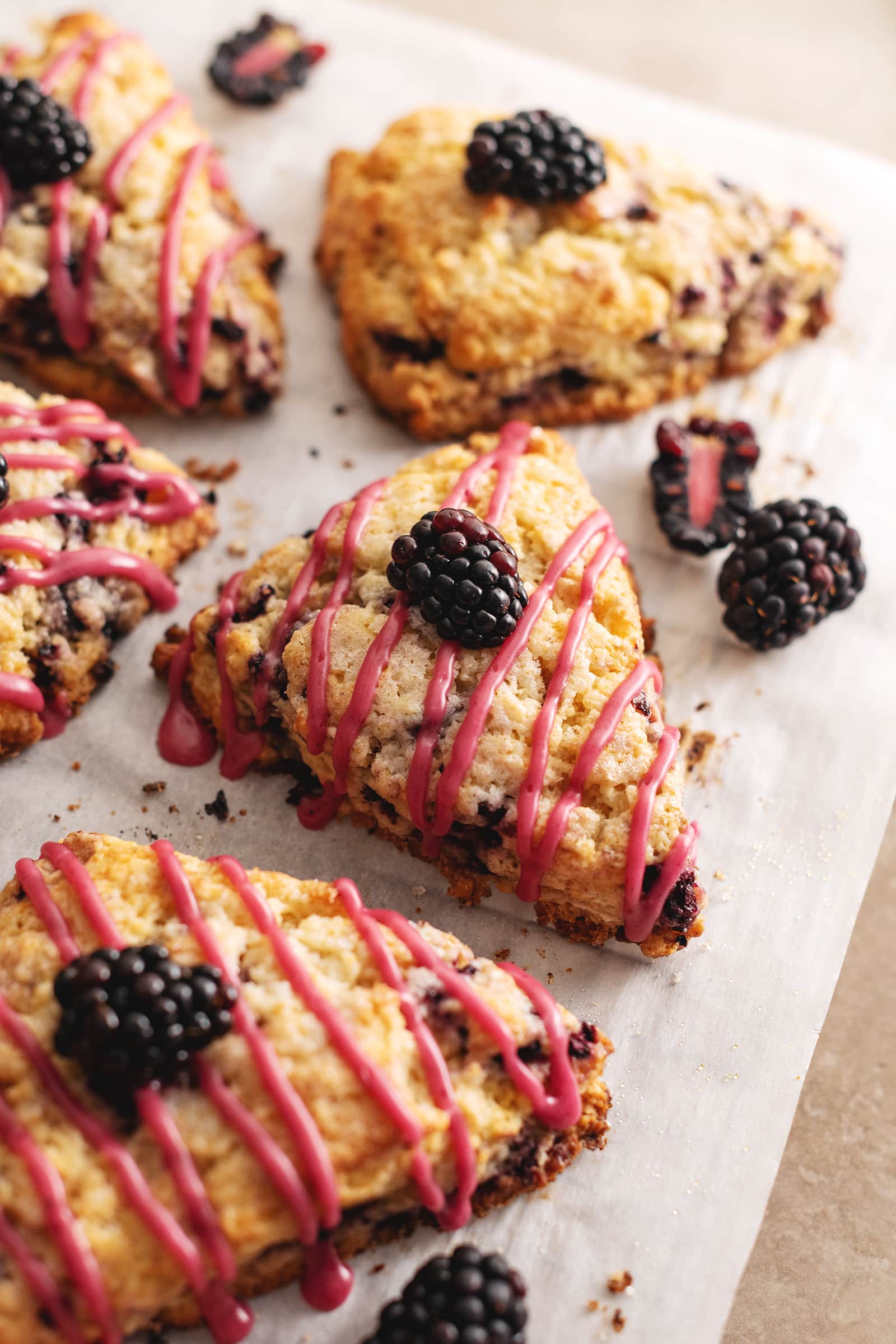 A blackberry scone with a drizzle of pink icing on parchment paper.