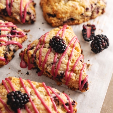 A blackberry scone with a drizzle of pink icing on parchment paper.