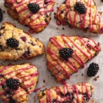 Several blackberry scones with drizzles of pink icing scattered on parchment paper.