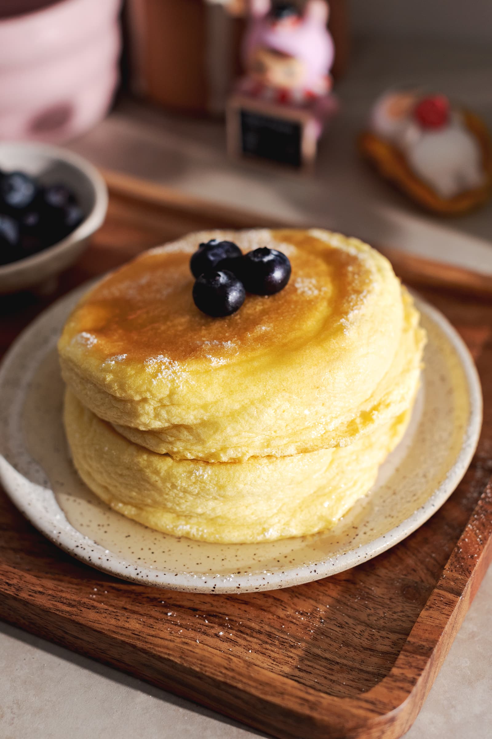 A stack of two Japanese souffle pancakes with blueberries on top on a plate and wooden tray.