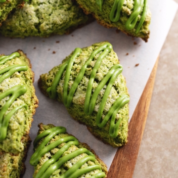 Matcha scones drizzled with matcha icing scattered on a wooden board.