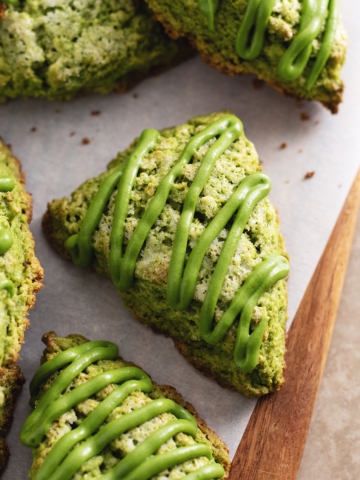 Matcha scones drizzled with matcha icing scattered on a wooden board.