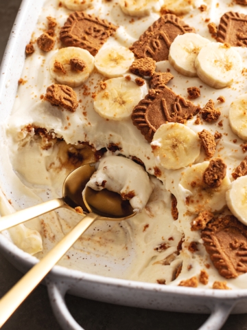 Two spoons in a serving dish of biscoff banana pudding where a section has been scooped out.