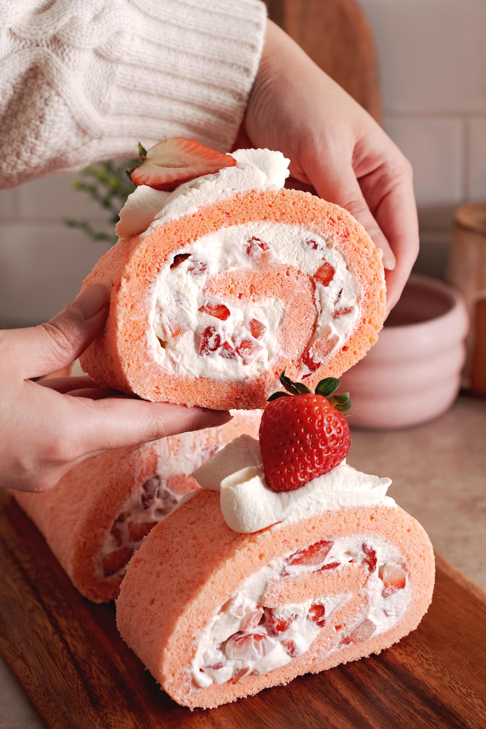 Hands lifting a slice of strawberry roll cake above the rest of the slices.