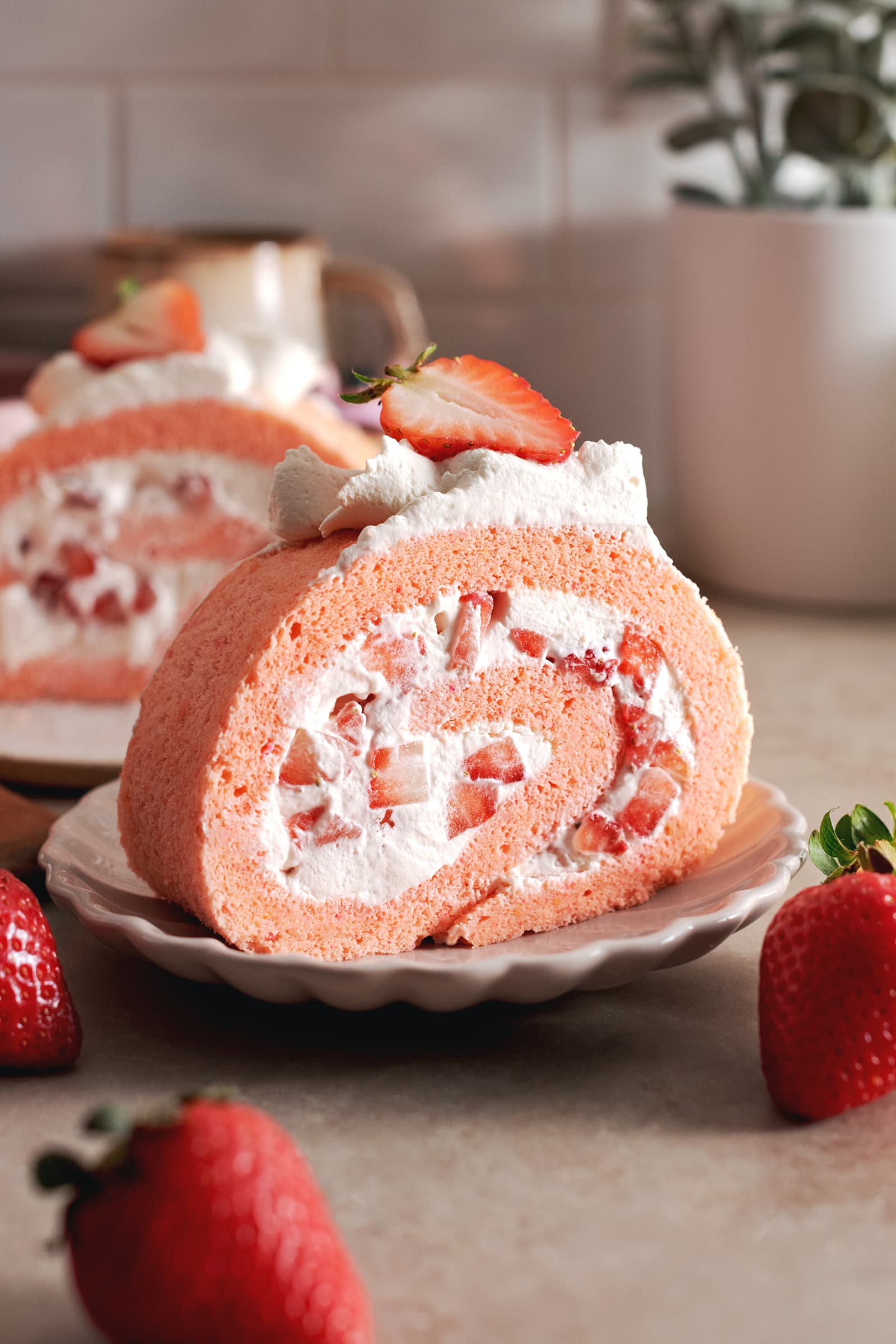 A slice of strawberry swiss roll cake rolled up with chunks of strawberries on a plate.