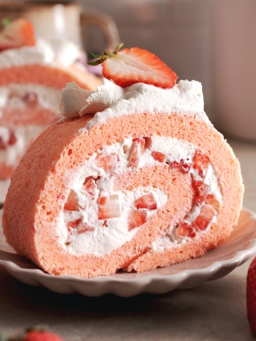 A slice of strawberry swiss roll cake rolled up with chunks of strawberries on a plate.