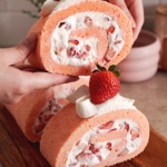 Hands lifting a slice of strawberry roll cake above the rest of the slices.
