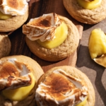 Several lemon meringue cookies topped with dollops of toasted meringue scattered on a wooden board.