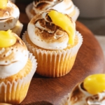 Close up of a lemon meringue cupcake with lemon curd dripping down the side of the toasted meringue.