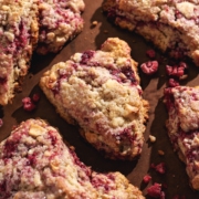 White chocolate raspberry scones scattered on a brown surface.