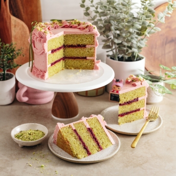 A raspberry pistachio cake on a cake stand with slices of cake on plates around it.