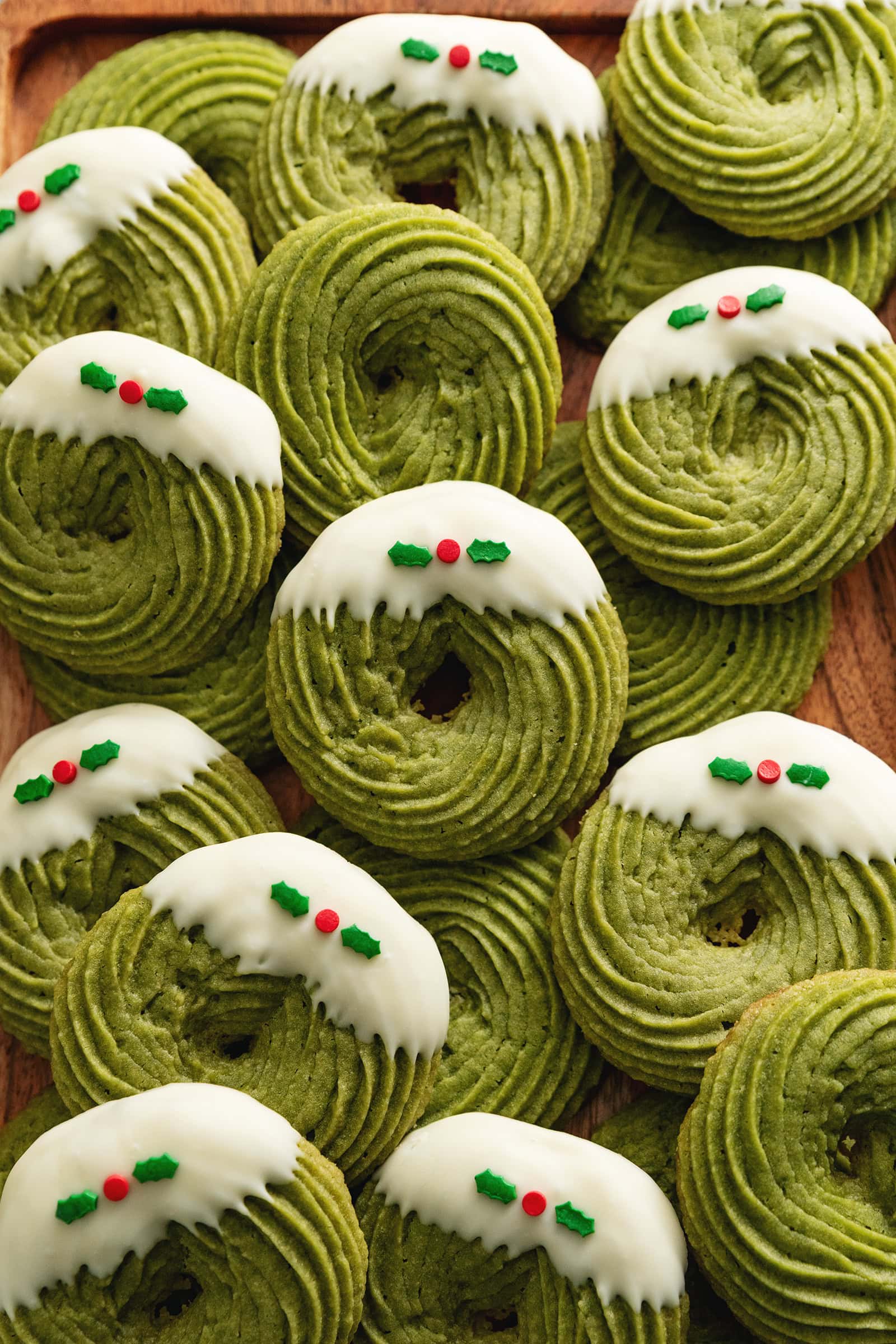 Several matcha butter cookies scattered and overlapping on a wooden tray.