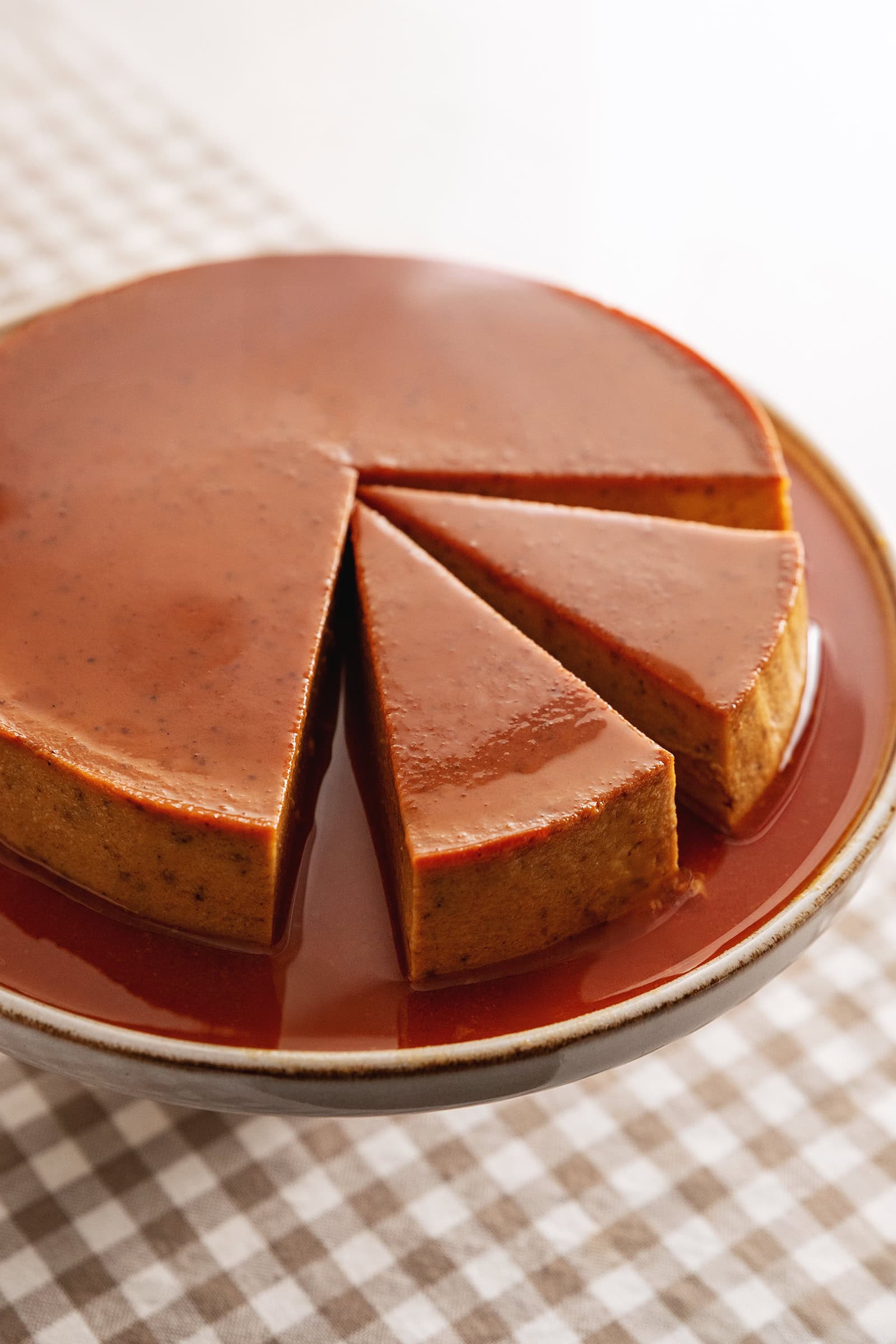 A pumpkin flan on a cake stand with two slices cut out of it.